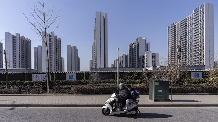 China Vanke Co. Isle Maison 개발 현장에서 건설 중인 고층 주거 건물들과 전경에서 스쿠터를 타고 있는 두 사람.