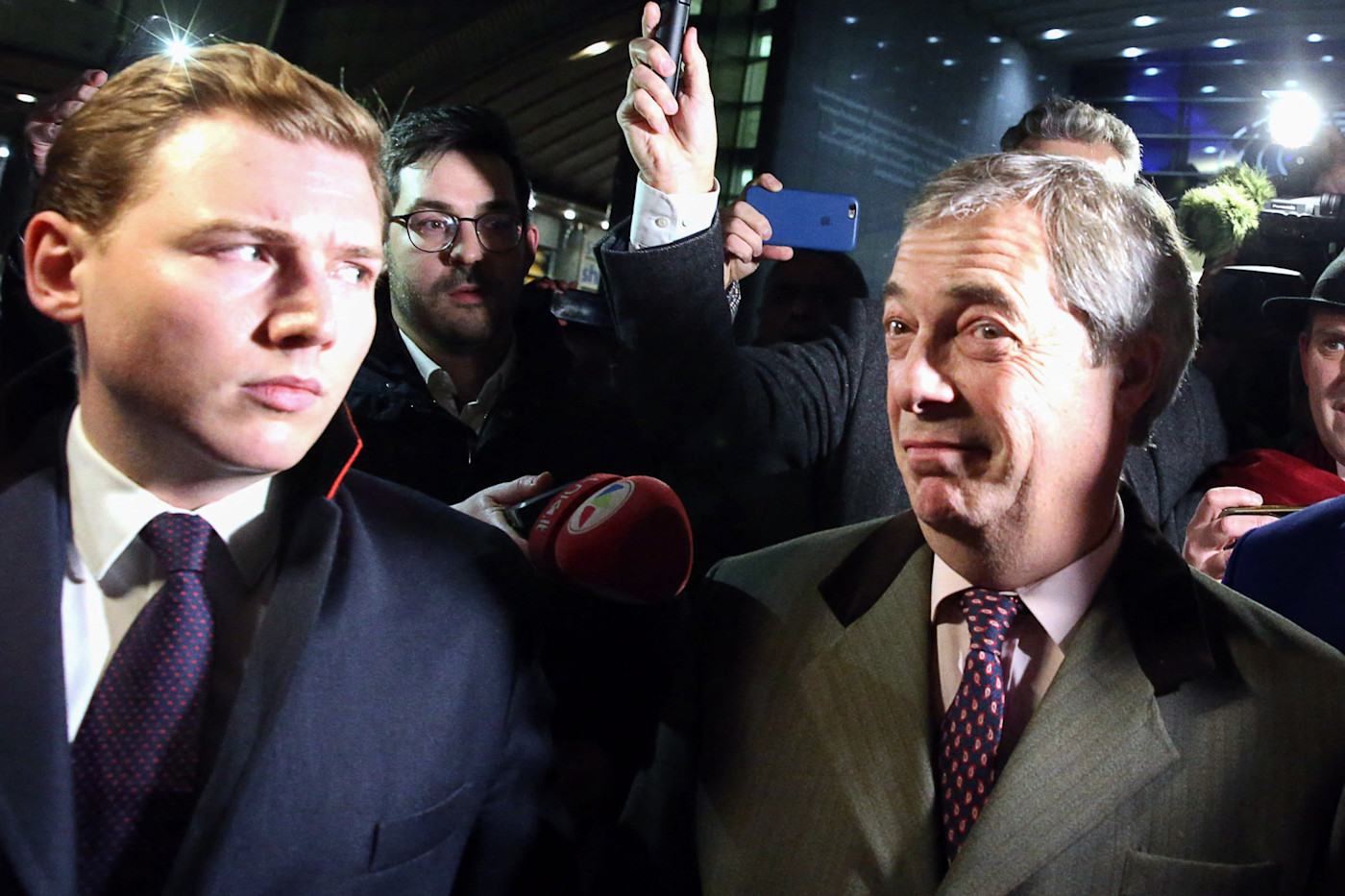 나이절 패라지와 조지 코트렐이 유럽의회 밖에서 기자와 사진기자들 사이를 걷고 있다.