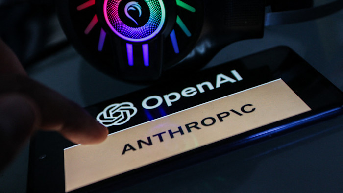 스마트폰 화면에 OpenAI 로고와 “Anthropic”이라는 문구가 표시되어 있고, 옆에는 여러 색상의 불빛이 켜진 헤드셋이 놓여 있다.