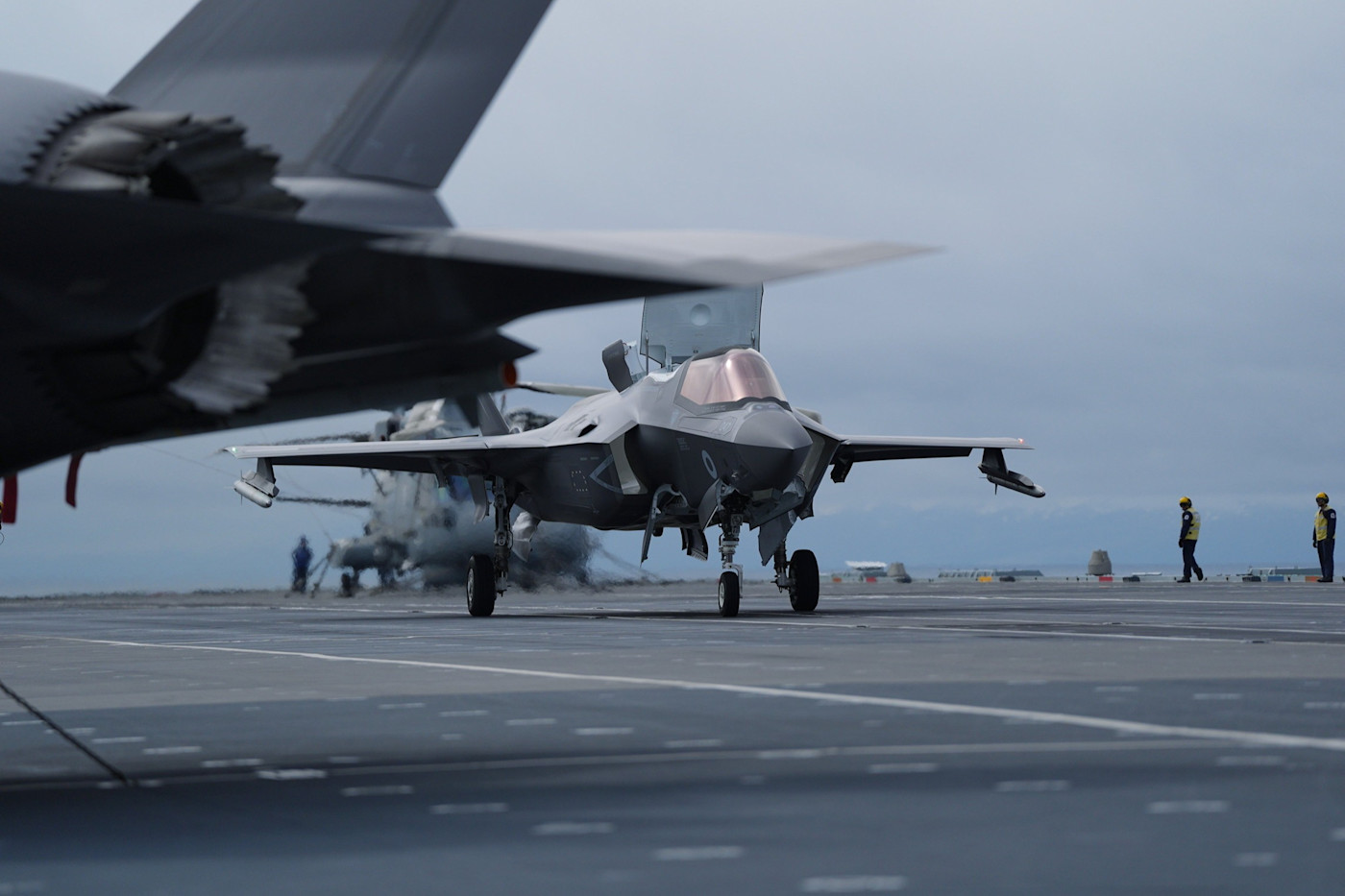 조종석을 연 채 이륙을 준비하는 F-35B 전투기가 HMS Prince of Wales 갑판에 있고 주변에 승무원들이 서 있다.