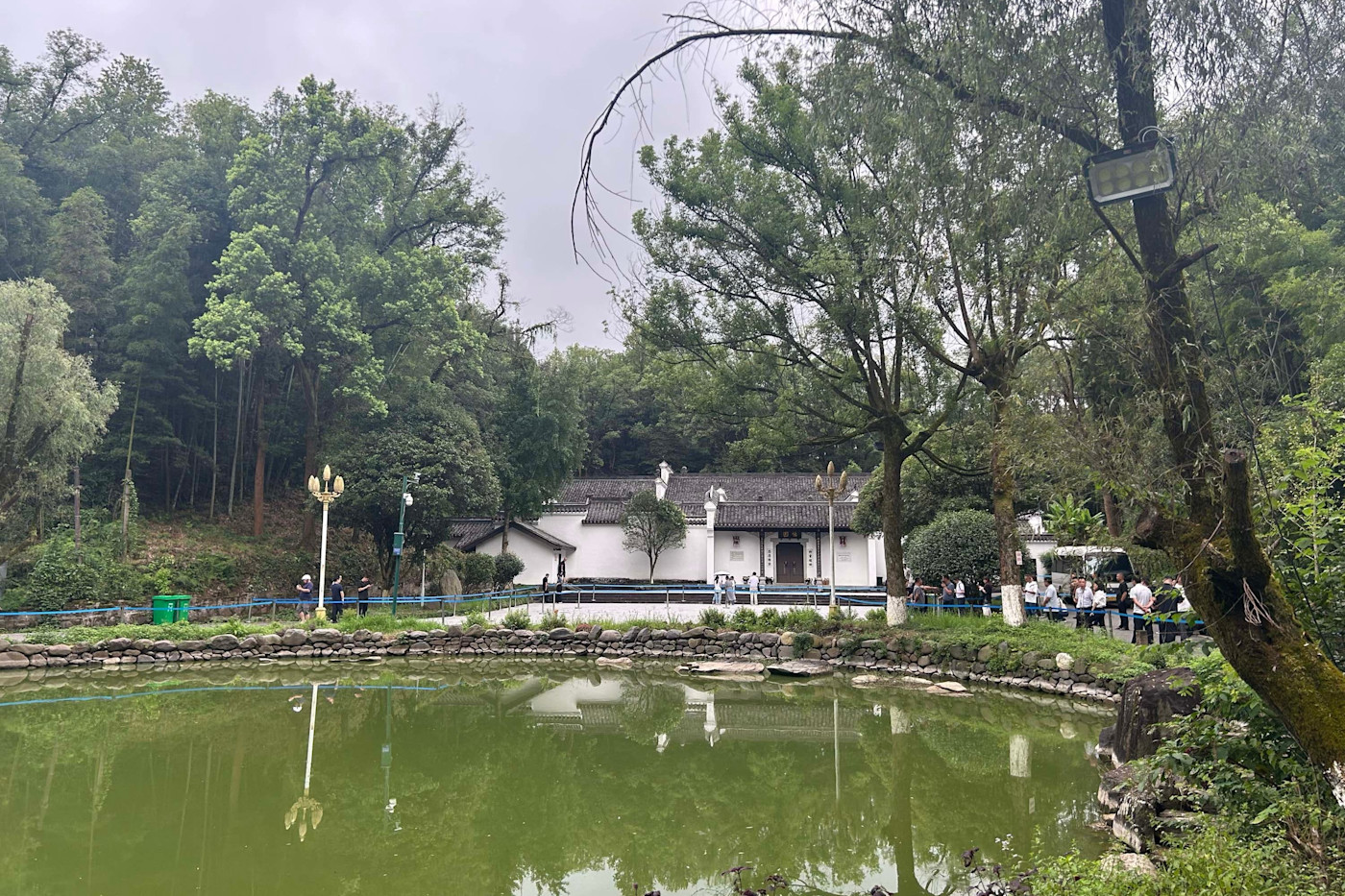 중국 허핑에서 나무와 연못으로 둘러싸인 Zhu Rongji의 흰 벽 주택 밖에 사람들이 모여 헌화하고 있다.