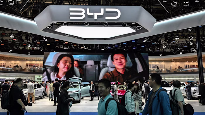 베이징 모터쇼의 BYD 부스에서 차량이 전시되고 대형 화면에 차 안의 두 사람이 비치는 가운데 사람들이 둘러보고 있다.