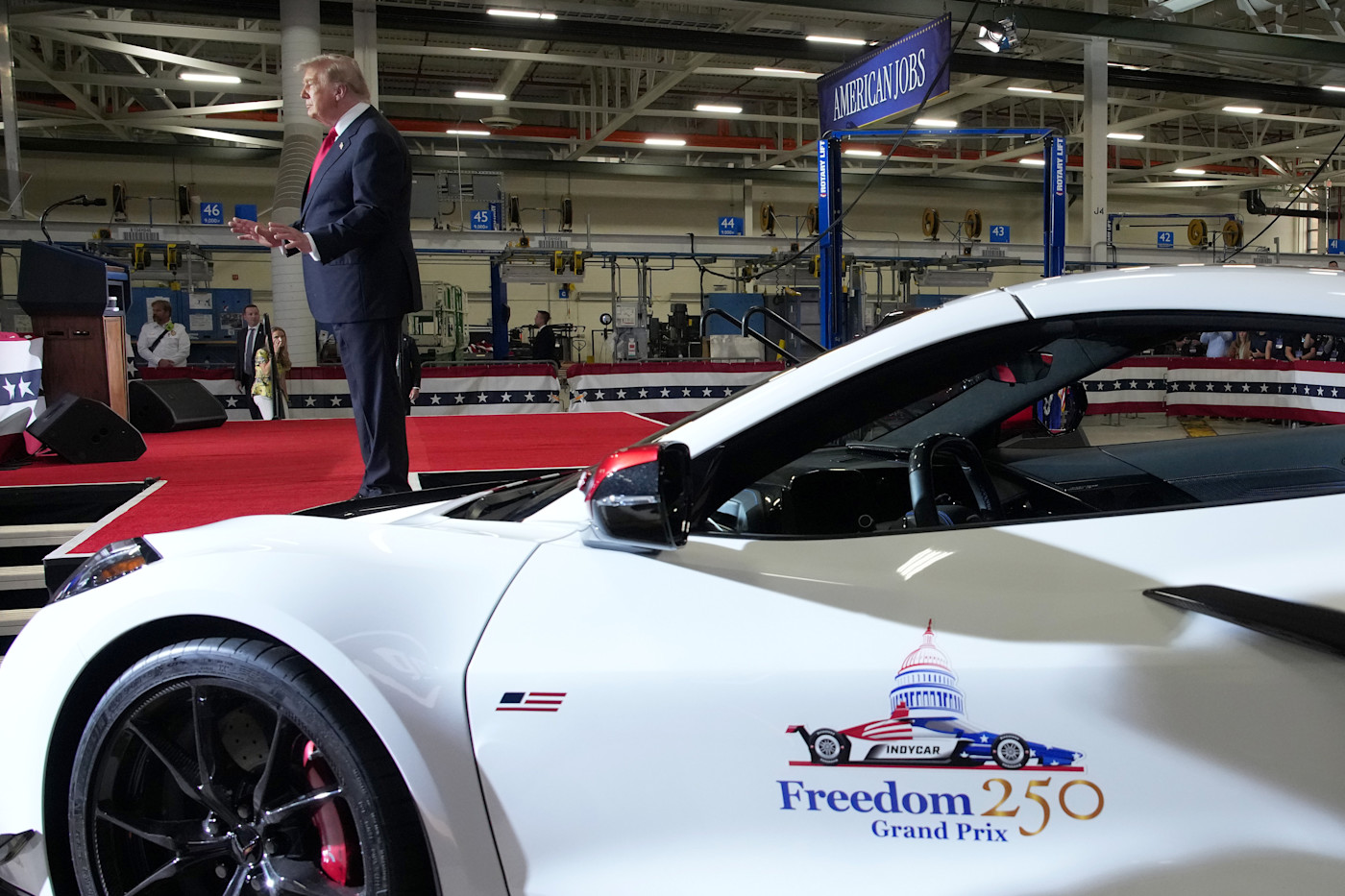 Donald Trump이 General Motors 공장 무대에서 “Freedom 250 Grand Prix”라고 표시된 흰색 스포츠카 근처에서 연설하고 있다.