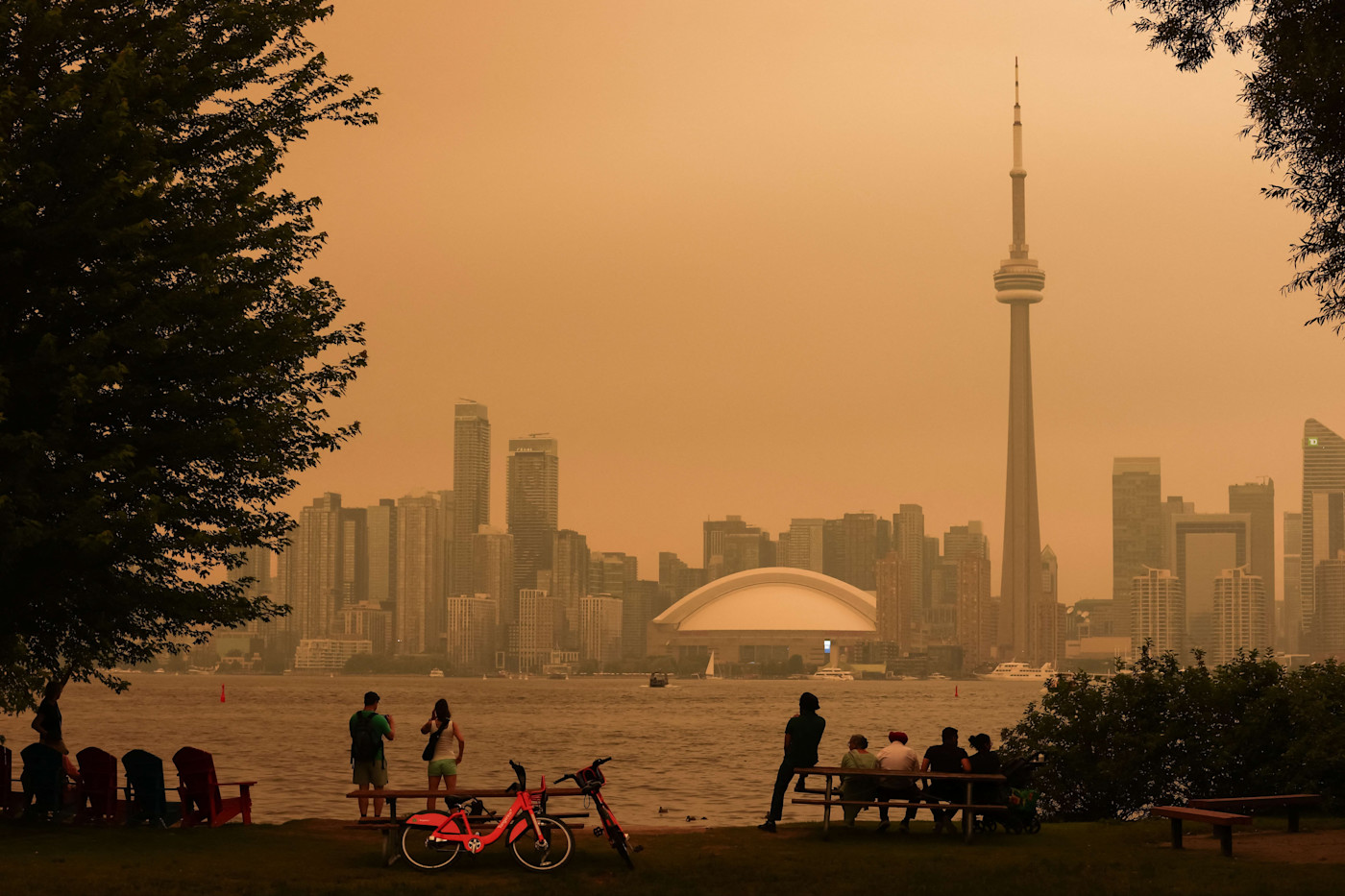 토론토 아일랜즈에서 사람들이 산불 연기로 짙은 노란 연무에 뒤덮인 도시 스카이라인을 물 건너 바라보고 있다.
