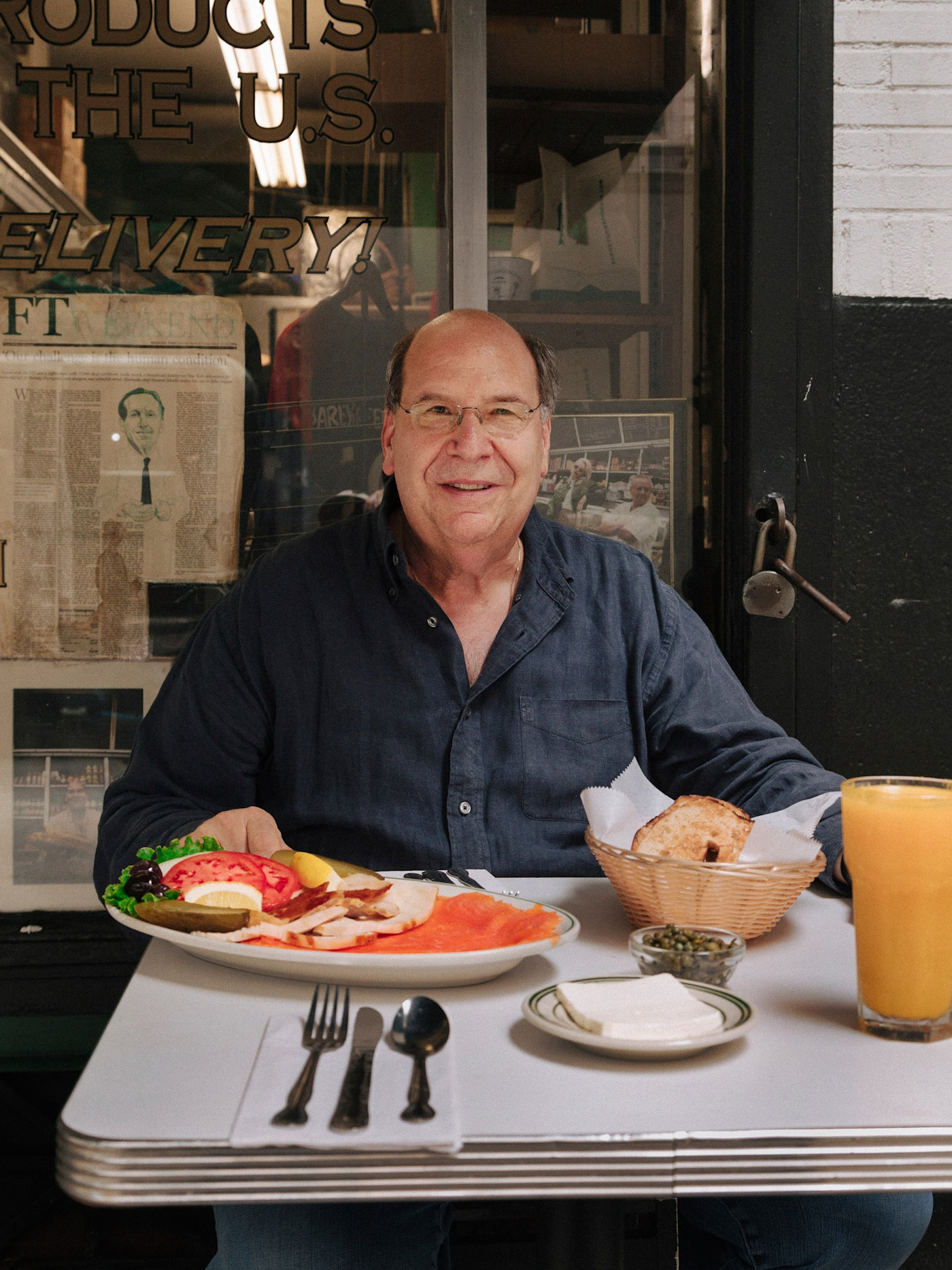 Gary Greengrass가 Barney Greengrass의 테이블에 앉아 훈제 생선, 빵, 케이퍼, 오렌지주스가 담긴 접시와 오렌지주스 한 잔을 앞에 두고 있다.