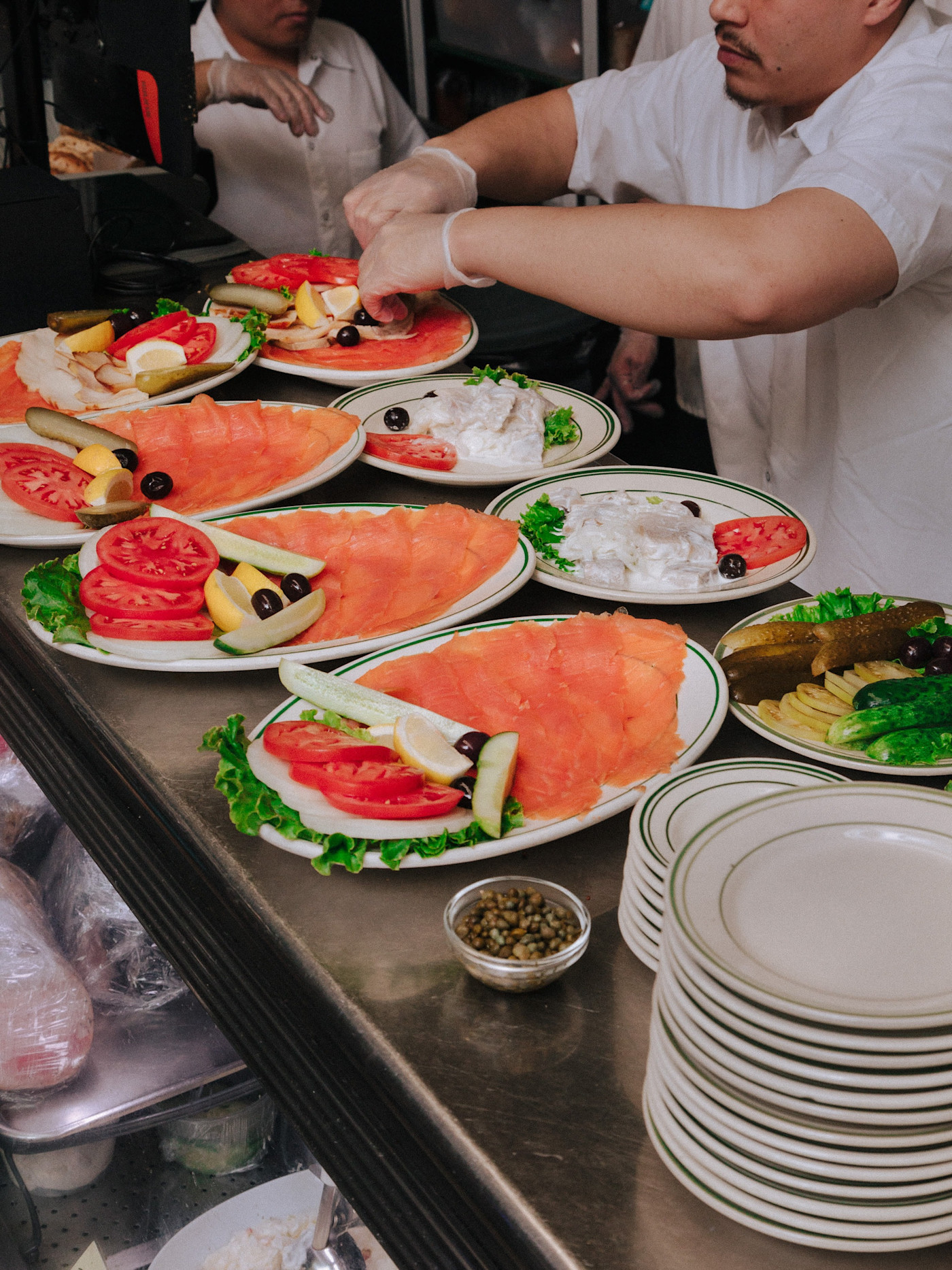 바니 그린그래스 직원들이 토마토, 양파, 레몬, 올리브, 피클과 함께 얇게 썬 훈제 연어를 여러 접시에 준비하고 있다.