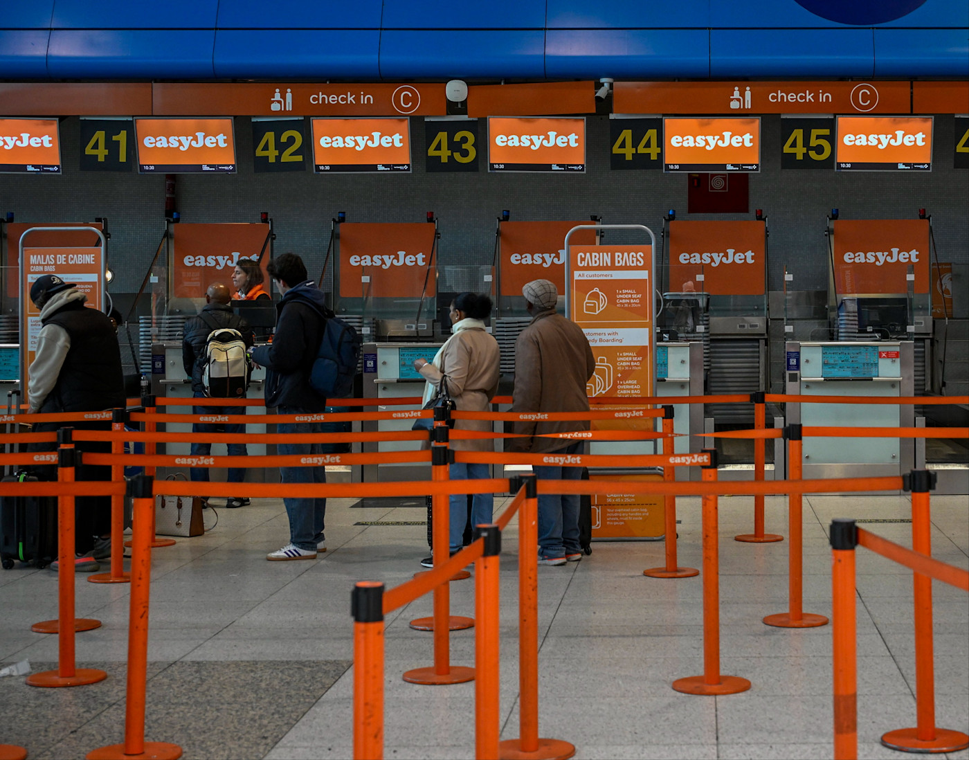리스본공항 제1터미널 이지젯 체크인 카운터에서 여행객들이 주황색 차단봉 사이로 짐을 들고 줄 서 있다.