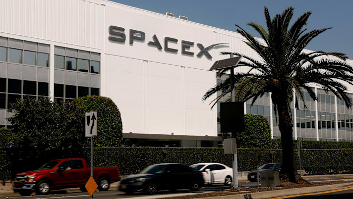 흰색 건물 외벽의 SpaceX 로고와 앞쪽의 야자수, 지나가는 차량들