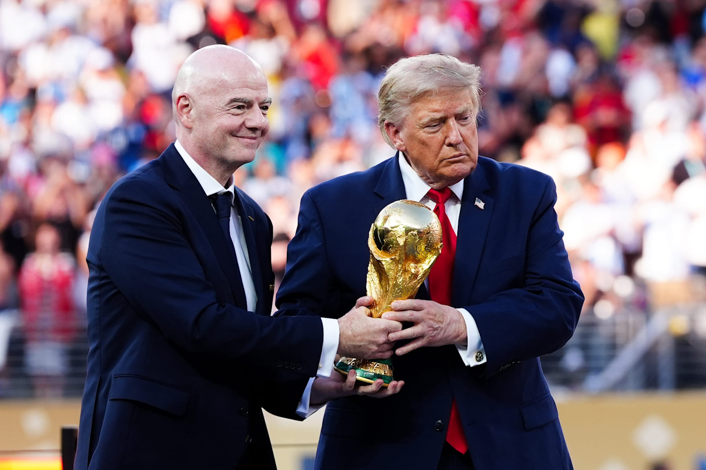 Gianni Infantino와 Donald Trump가 행사에서 어두운색 정장을 입고 FIFA 월드컵 트로피를 함께 들고 있다.