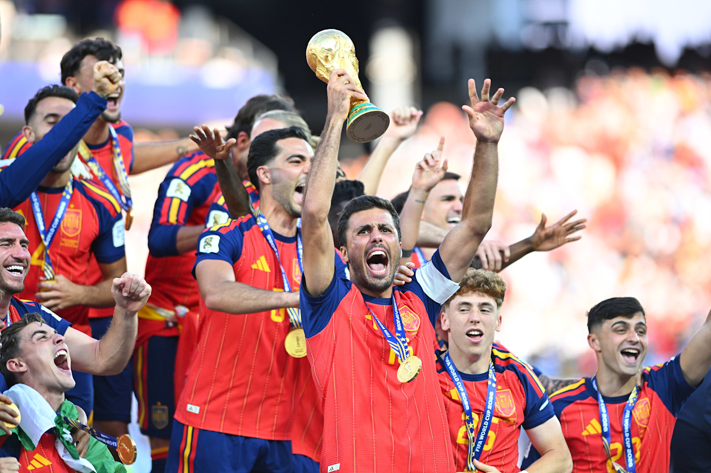 로드리가 메달을 목에 건 스페인 동료들과 함께 우승을 축하하며 FIFA 월드컵 트로피를 들어 올리고 있다.