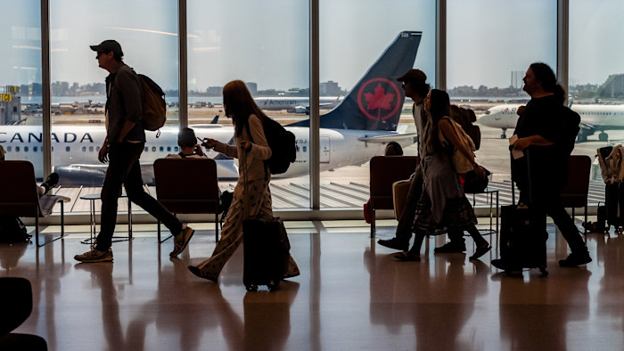 샌프란시스코 공항 게이트에서 여행객들이 에어캐나다 항공기를 내려다보는 대형 창문 옆으로 짐을 끌며 지나가고 있다.