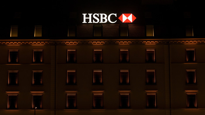 밤, HSBC 지점 건물 꼭대기에 불이 켜진 간판과 따뜻한 조명으로 윤곽이 드러난 아래쪽 창문들.