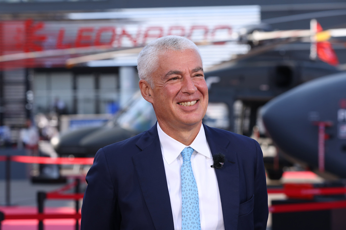 Farnborough International Airshow에서 TV 인터뷰 중 미소 짓는 Lorenzo Mariani. 뒤로 헬리콥터와 Leonardo 표지판이 보인다.