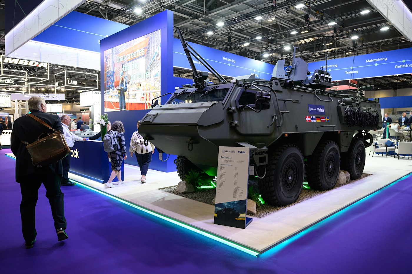 DSEI 런던에서 방문객들이 지나가는 가운데 전시장 부스에 Babcock Patria 6x6 장갑차가 전시돼 있다.