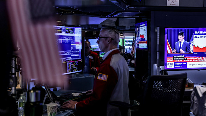 FOMC 회의 후 발언하는 Kevin Warsh가 TV 화면에 보이는 가운데, 트레이더들이 NYSE 객장에서 업무를 보고 있다.