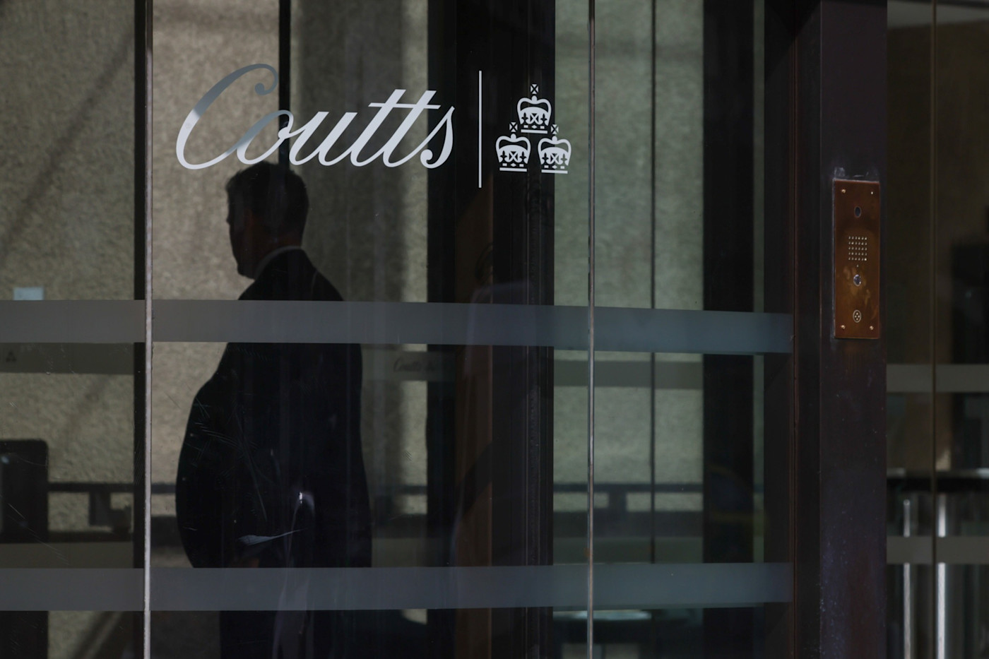 Coutts & Co 본사 유리문에 있는 로고와 안쪽에 보이는 사람의 실루엣.