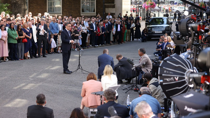 UK 총리가 된 Andy Burnham이 다우닝가 10번지 밖 연단에서 대규모 군중과 모인 언론을 마주하며 연설하고 있다.