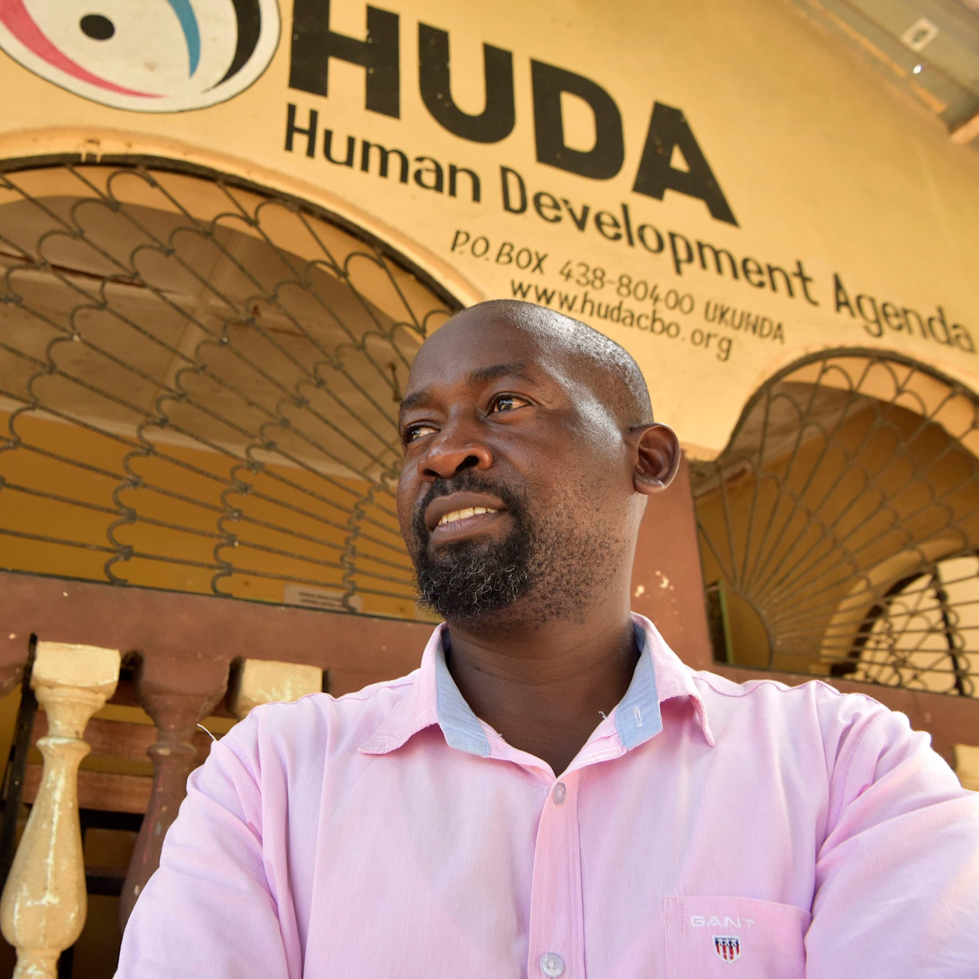핑크색 셔츠를 입은 저메인 카시가 우쿤다의 HUDA 인간개발 어젠다 건물 앞에 서 있다.