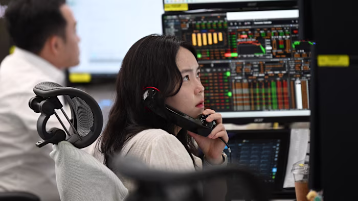 트레이딩룸에서 한 통화 딜러가 전화 통화를 하며 환율 데이터가 표시된 여러 화면을 지켜보고 있다.