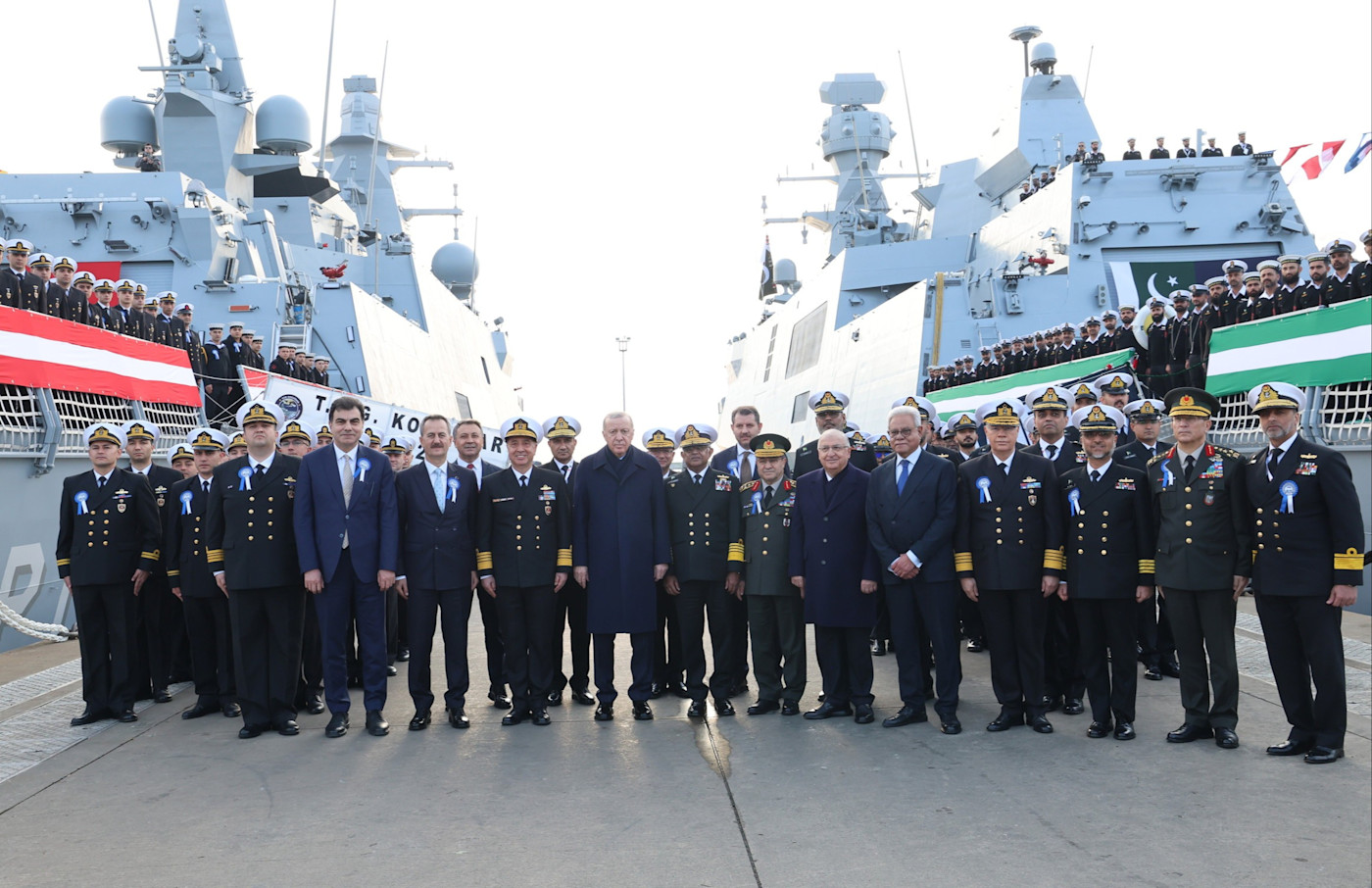 에르도안이 부두에서 고위 해군 관계자들과 귀빈들 사이에 서 있고, 양옆에 군함이 정박해 있다.