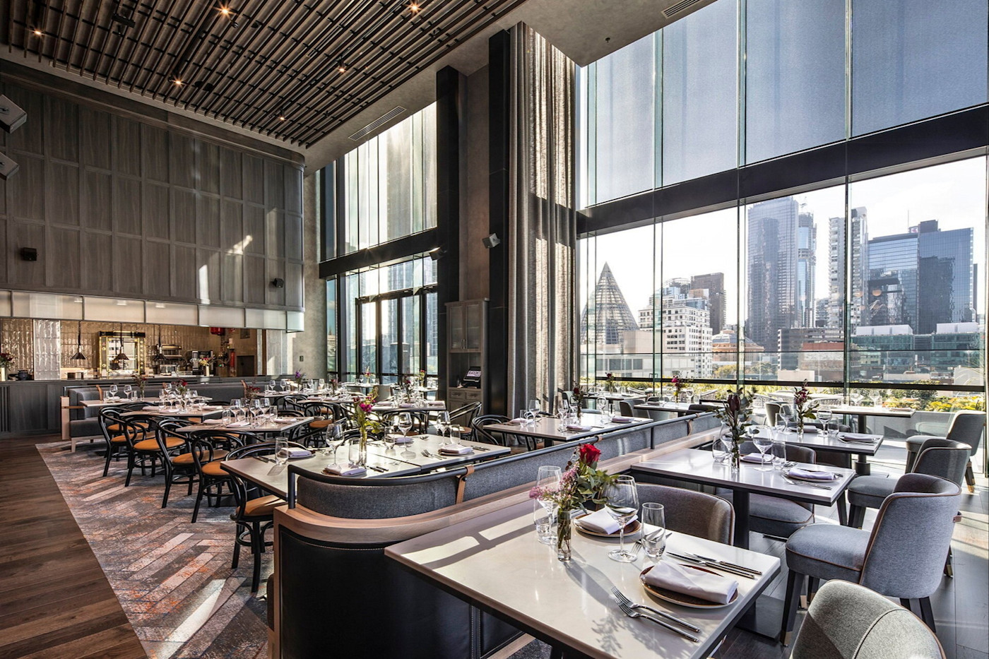 도시 스카이라인이 보이는 통유리창을 갖춘 호텔의 넓고 현대적인 Blacksmith Bar & Grill 레스토랑. 테이블에는 와인잔과 식기, 작은 꽃 장식이 놓여 있다.