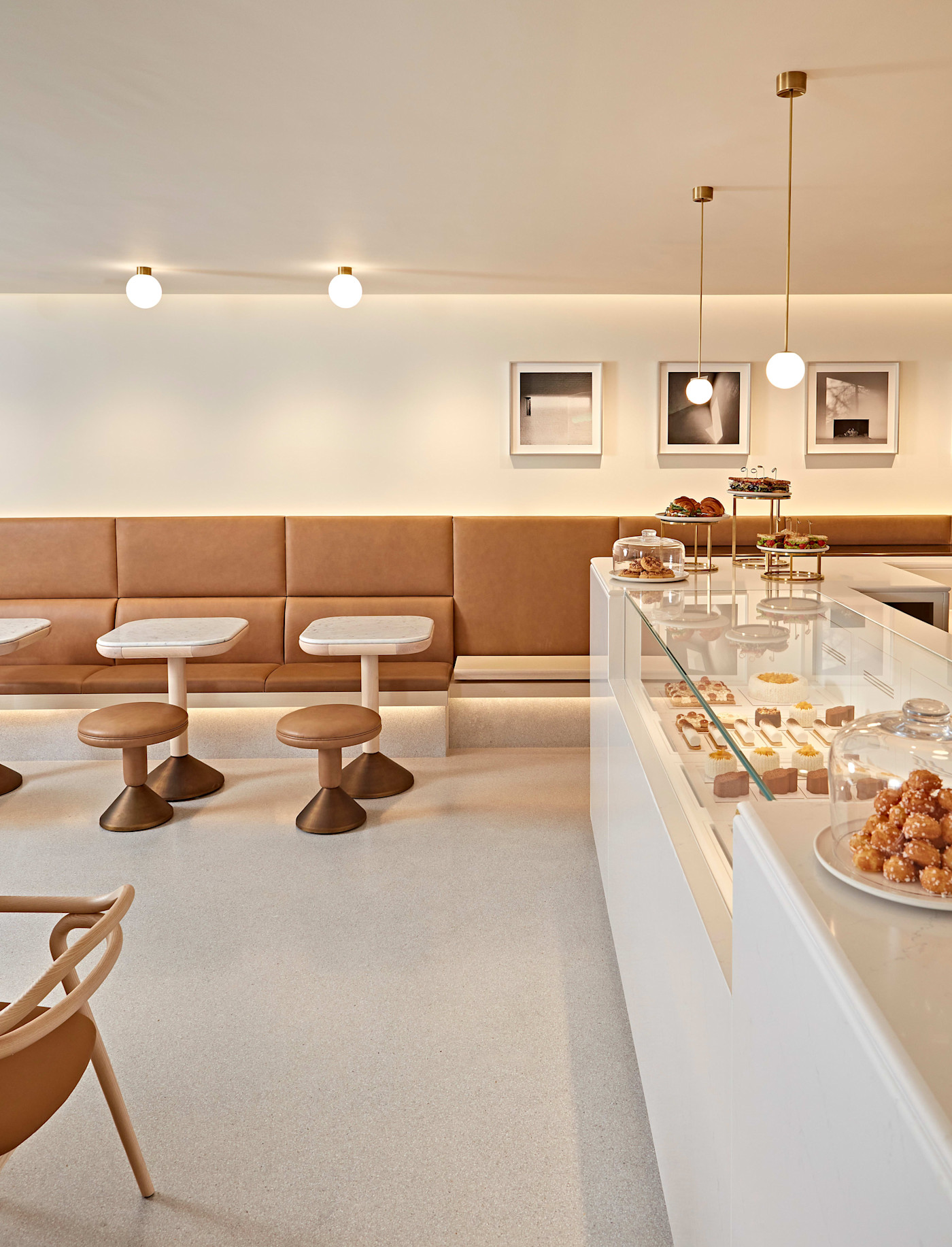 Claridge’s ArtSpace Café의 현대적이고 미니멀한 내부 모습. 황갈색 가죽 좌석과 작은 원형 테이블, 페이스트리와 디저트가 가득한 진열장이 보인다. 크림색 벽의 붙박이 소파 위에는 액자에 담긴 미술 작품이 걸려 있다.