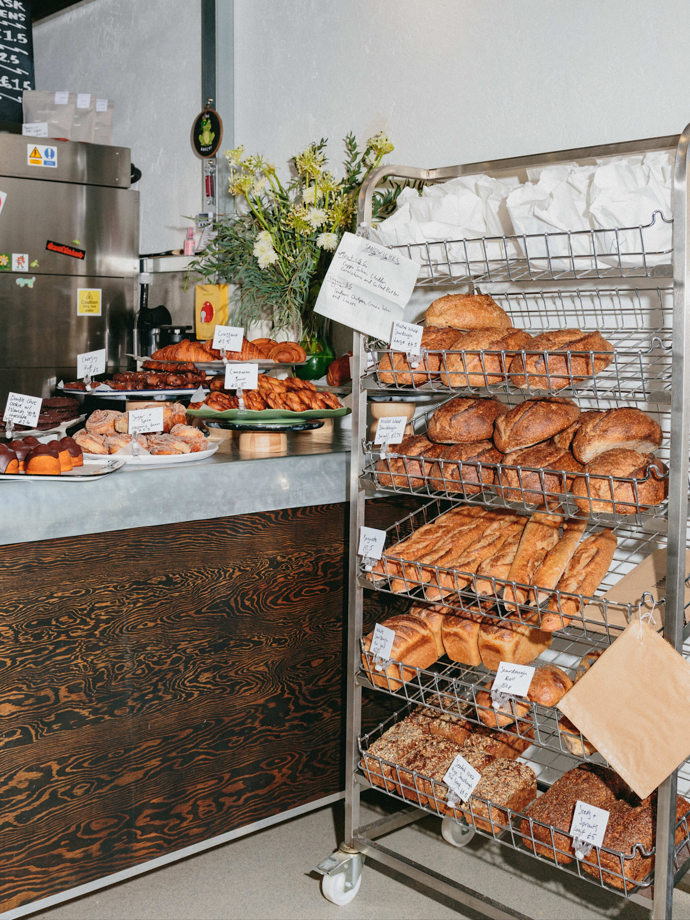 Toad Bakery의 다양한 빵이 진열된 선반과 페이스트리가 가득한 카운터, 손글씨 라벨과 꽃다발이 보이는 베이커리 매장.