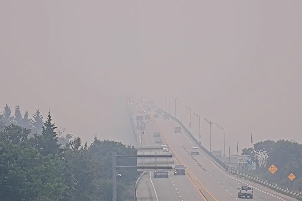짙은 산불 연기에 일부 가려진 Mackinac Bridge, 제한된 가시거리 속 여러 차량이 건너는 모습.