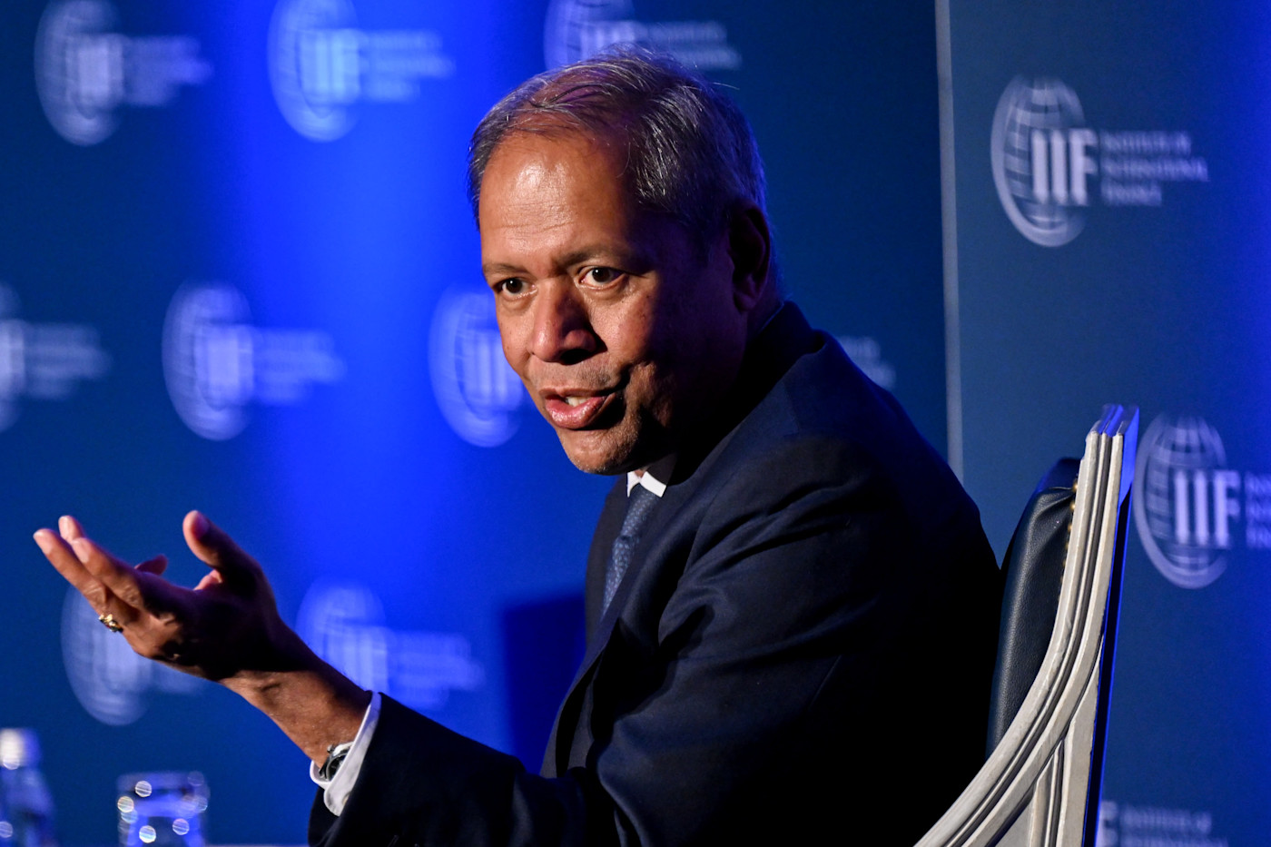 IIF 글로벌 전망 포럼에서 IIF 로고가 있는 배경 앞에 앉아 발언하며 제스처를 취하는 CS Venkatakrishnan.