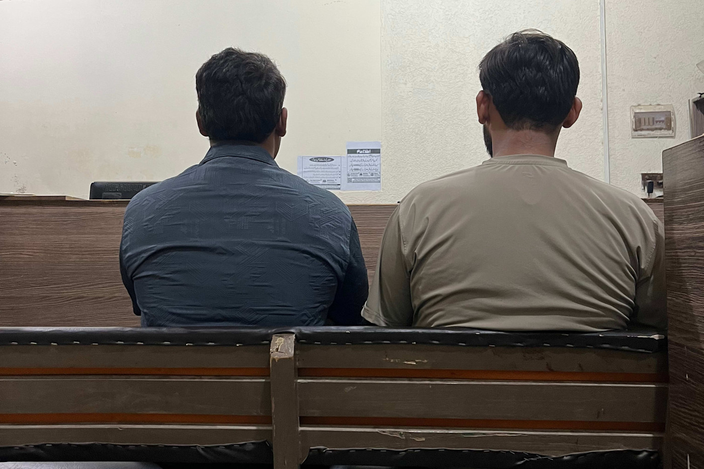 파란 셔츠를 입은 압둘 사맛이 왼쪽에 앉아 베이지색 셔츠를 입은 사촌 무함마드 사아드 옆에 있다. 두 사람 모두 뒷모습이다.