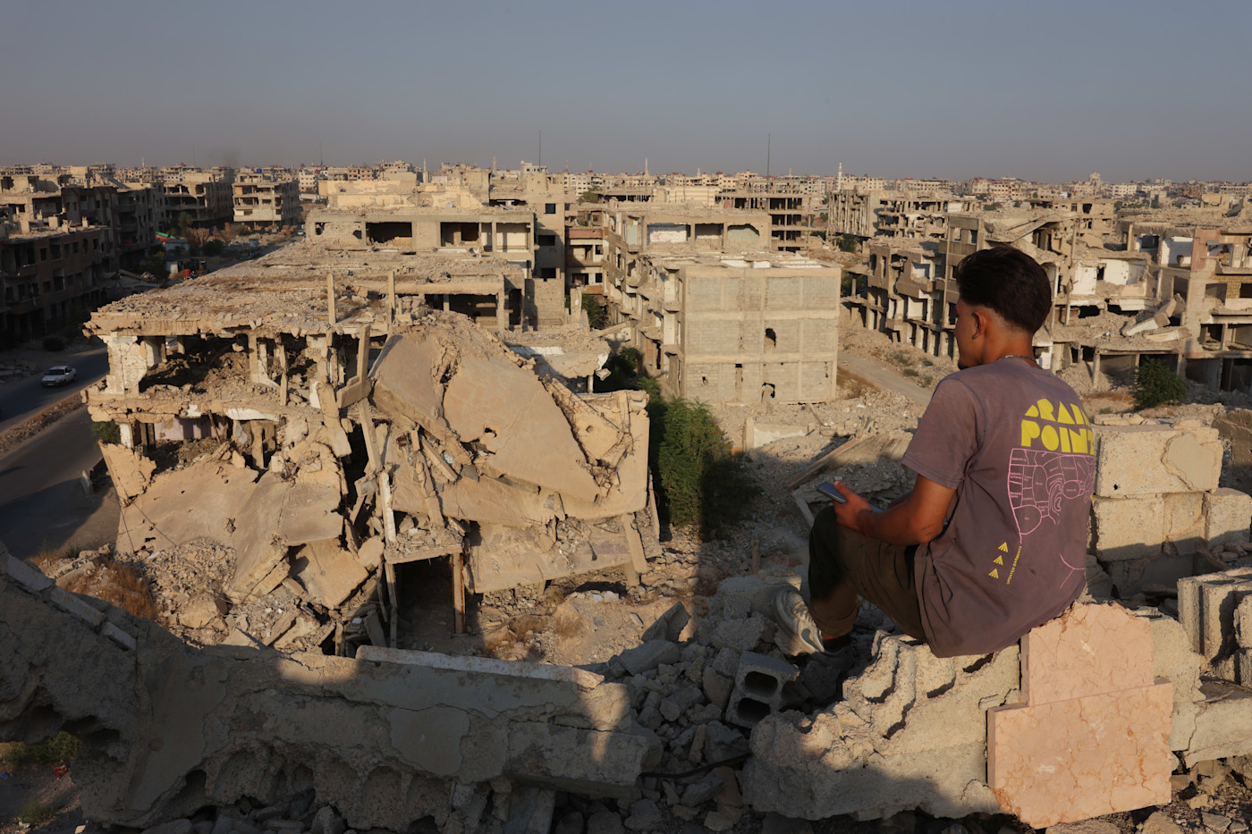 A young man sits on rubble overlooking heavily damaged and destroyed buildings in Jobar, Syria.