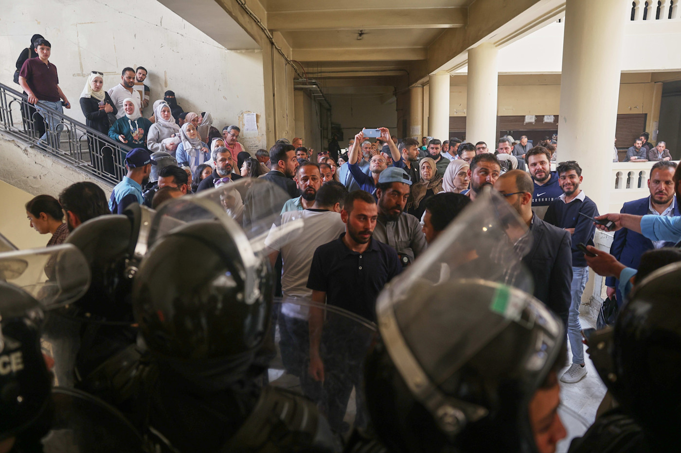 Riot police in helmets and shields block a hallway as a large crowd gathers inside the Palace of Justice during Atef Najib's first trial session.