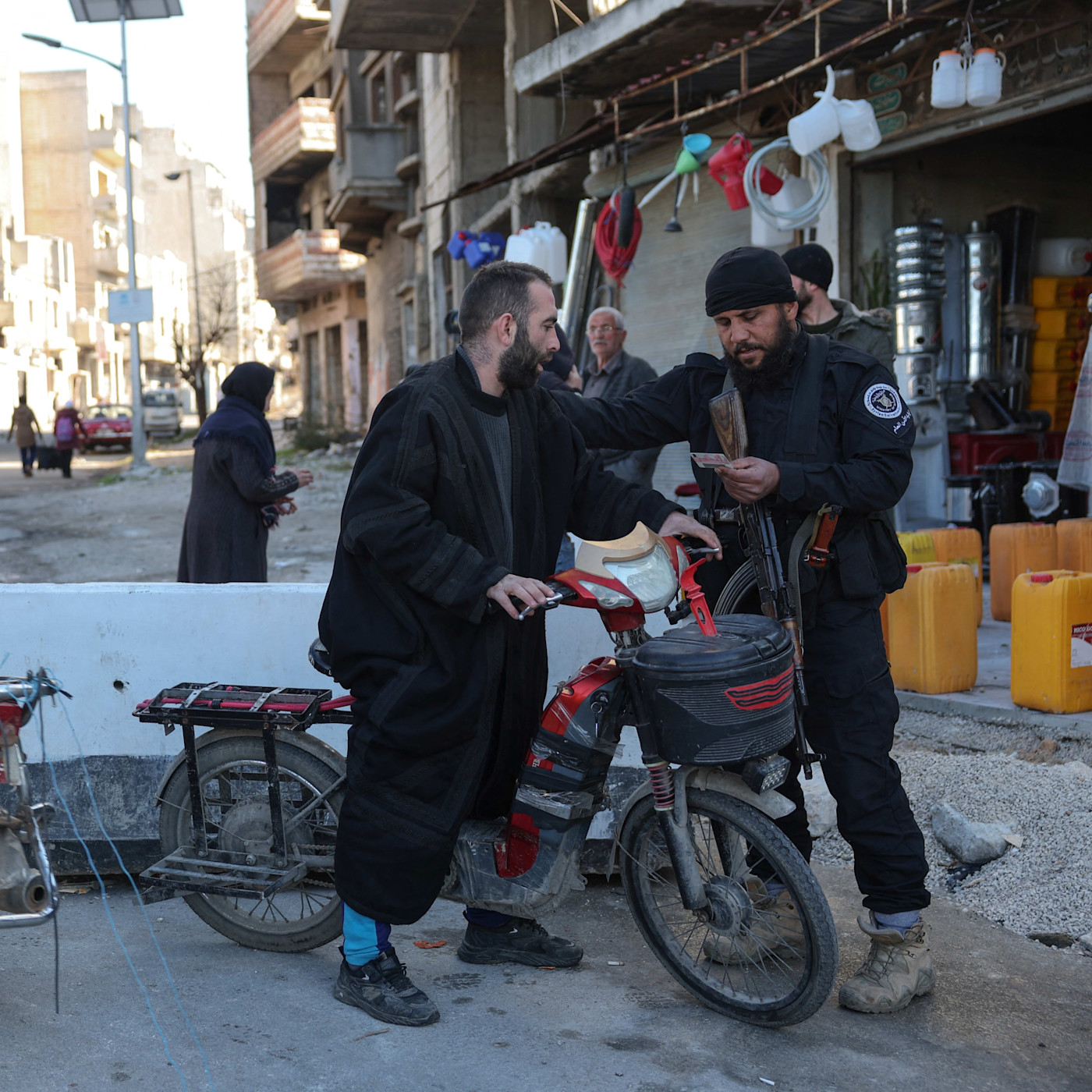 A security officer checks the identification of a man on a scooter at a street checkpoint in Homs, Syria.