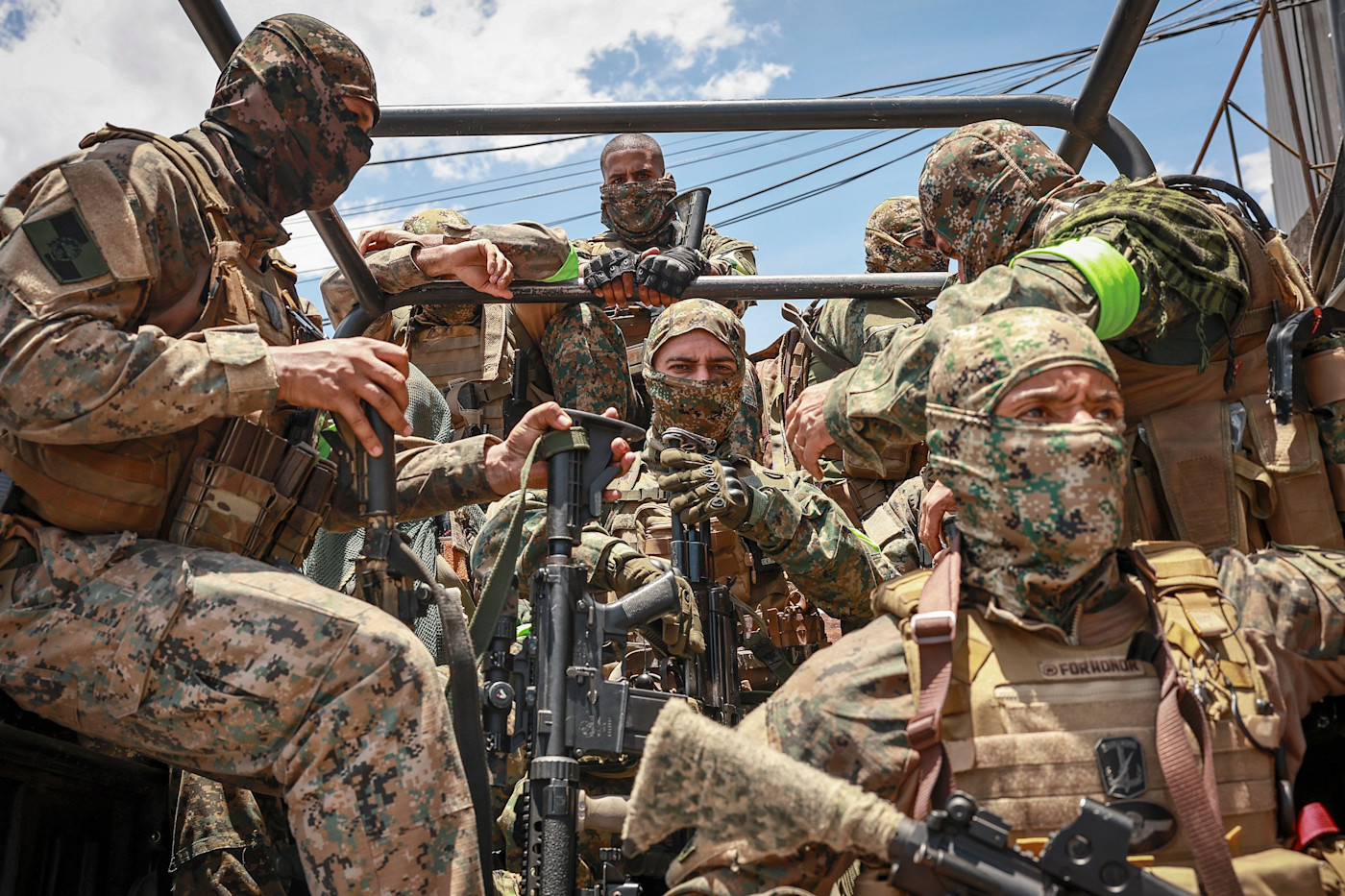 위장복과 방탄조끼를 입고 발라클라바로 얼굴을 가린 경찰들이 트럭 뒤에서 응시하고 있다